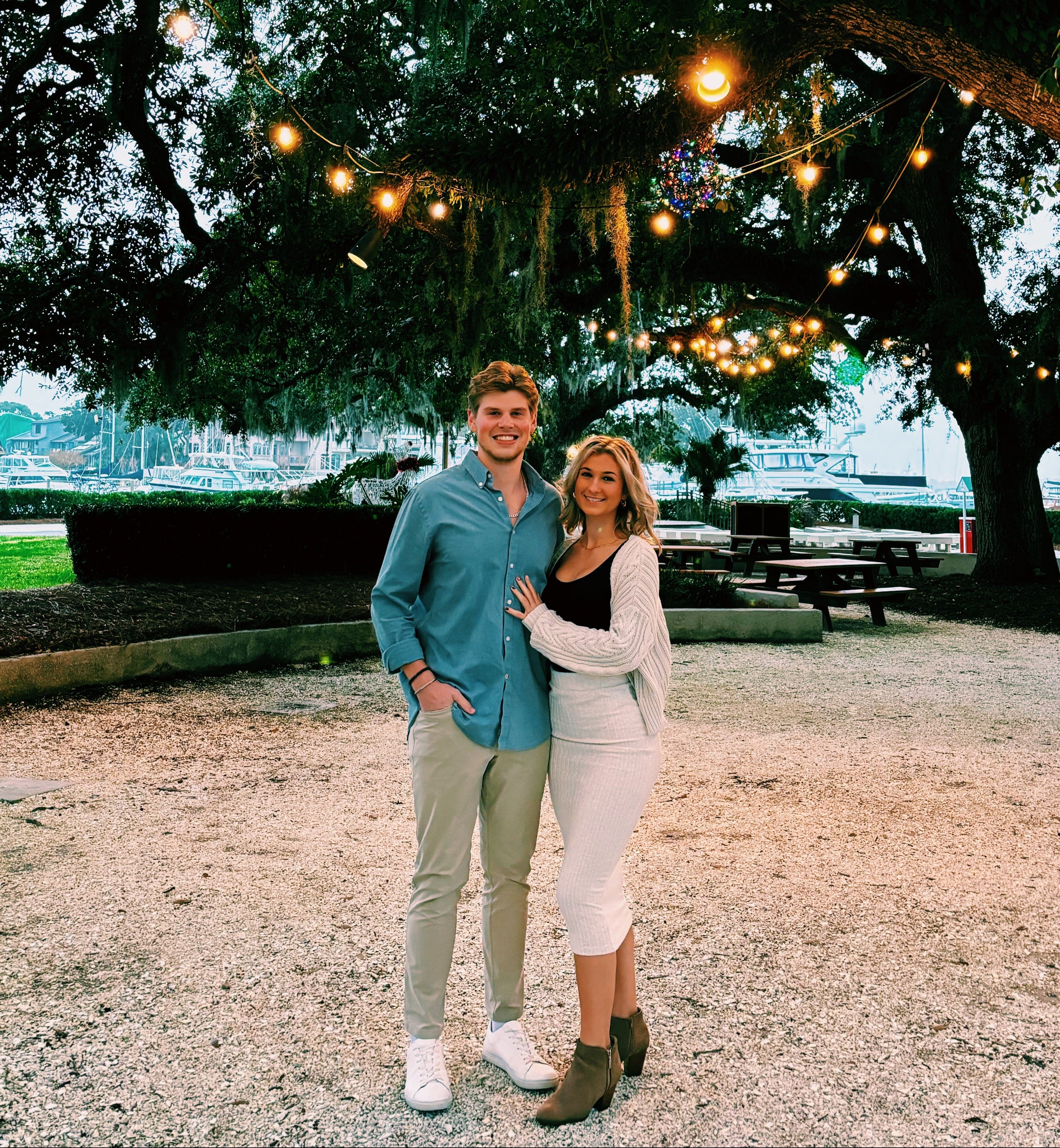 Josh and Chloe standing under a tree with string lights in an outdoor setting
